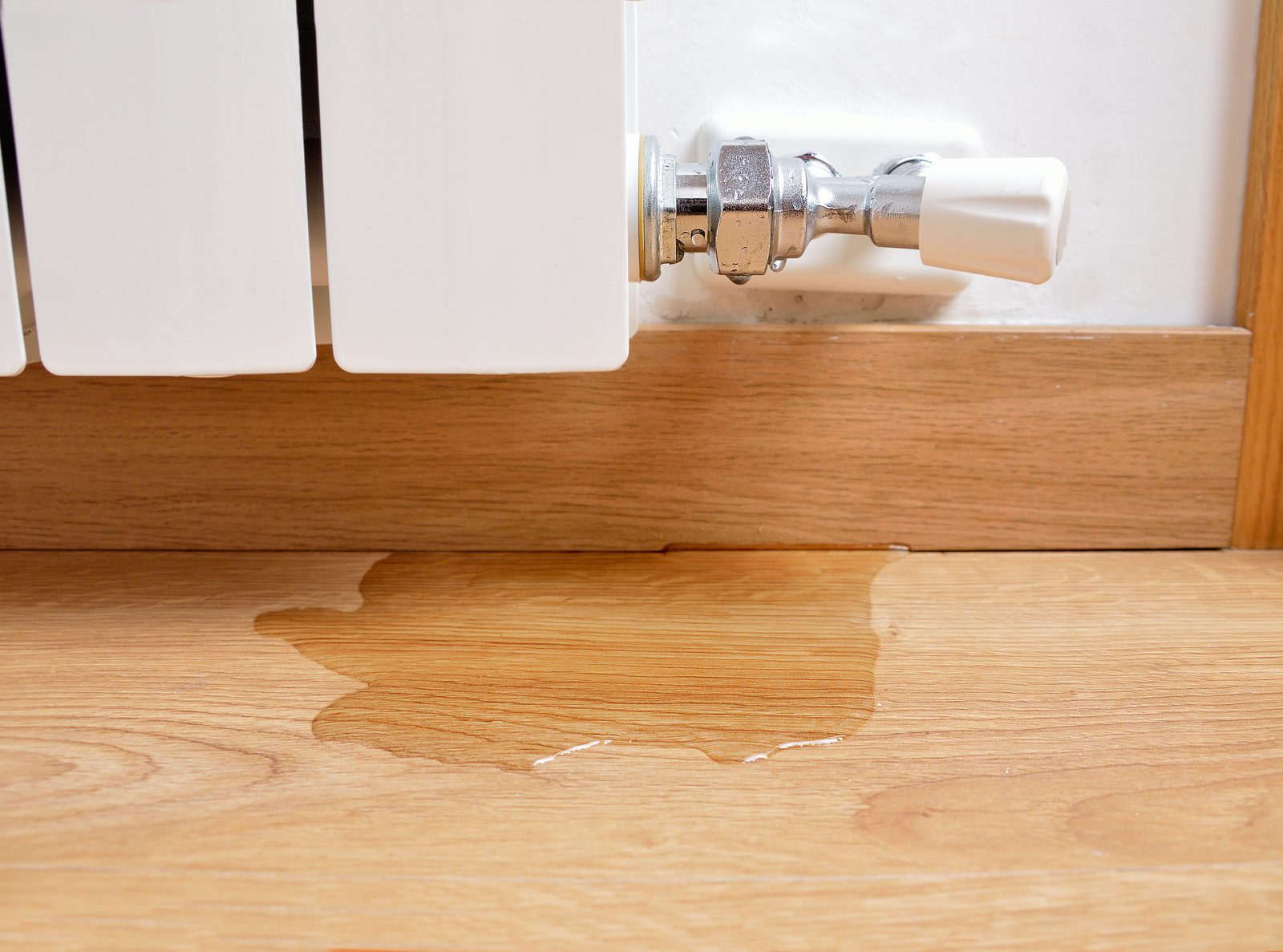 Water puddle on a wood floor below a radiator valve